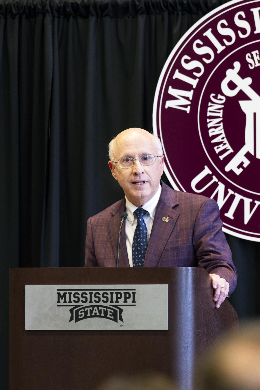 man in maroon blazer in front of podium