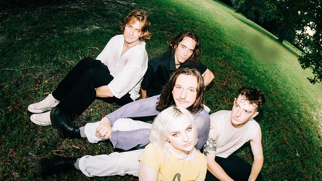 fisheye lens of five bandmates sitting on the grass
