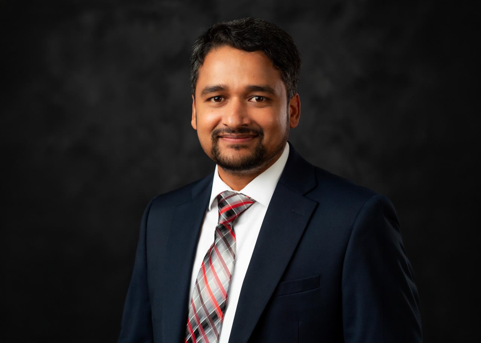 headshot of man in blazer and tie on black background