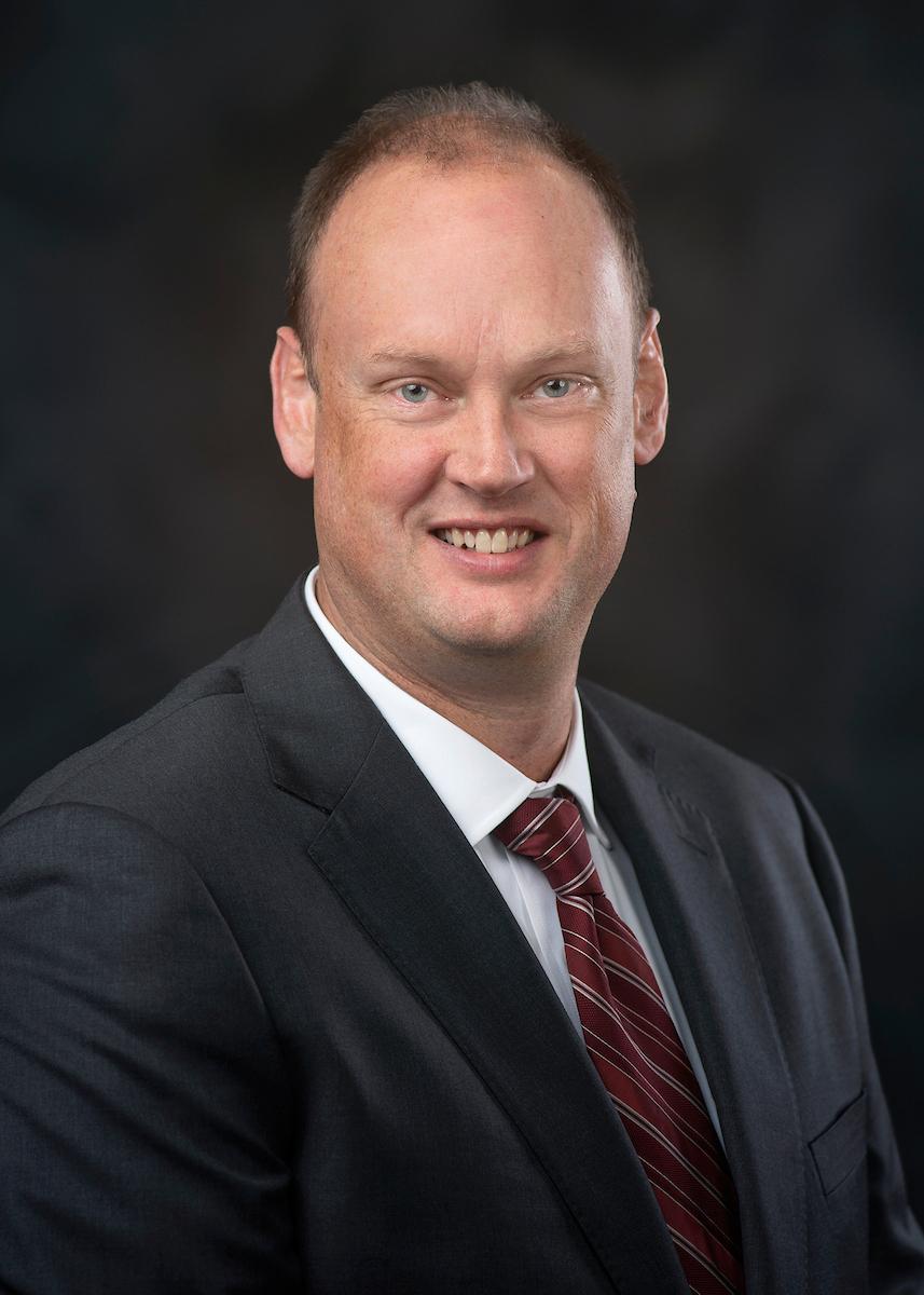 headshot of man in black suit on a black background