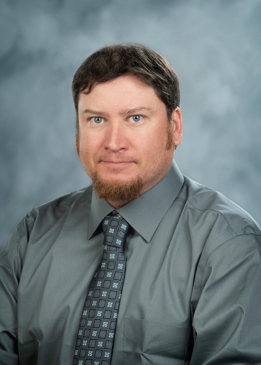 headshot of man in grey shirt on grey background