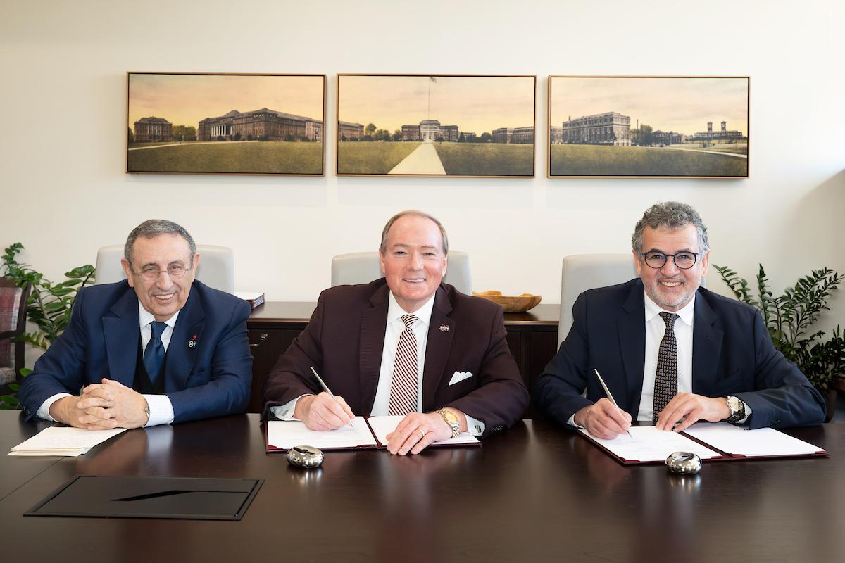 three men sit at table signing an MOU