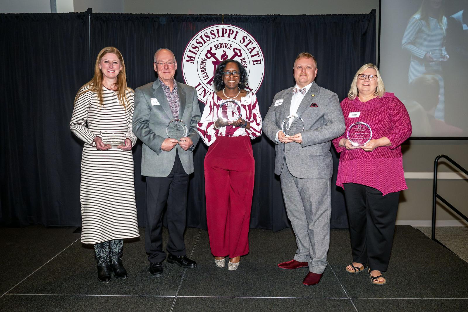 a group of award winners in front of a black curtain with a mississippi state seal
