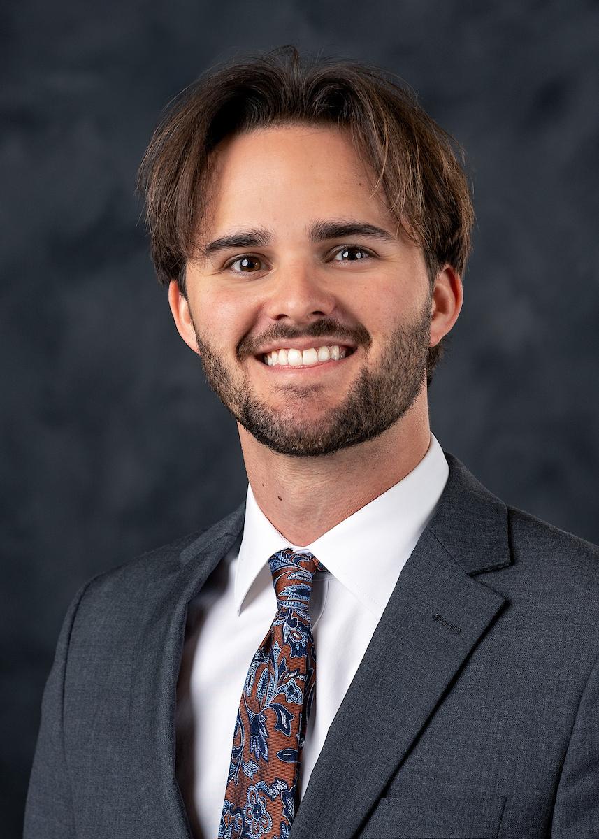 headshot of young man with beard on grey background