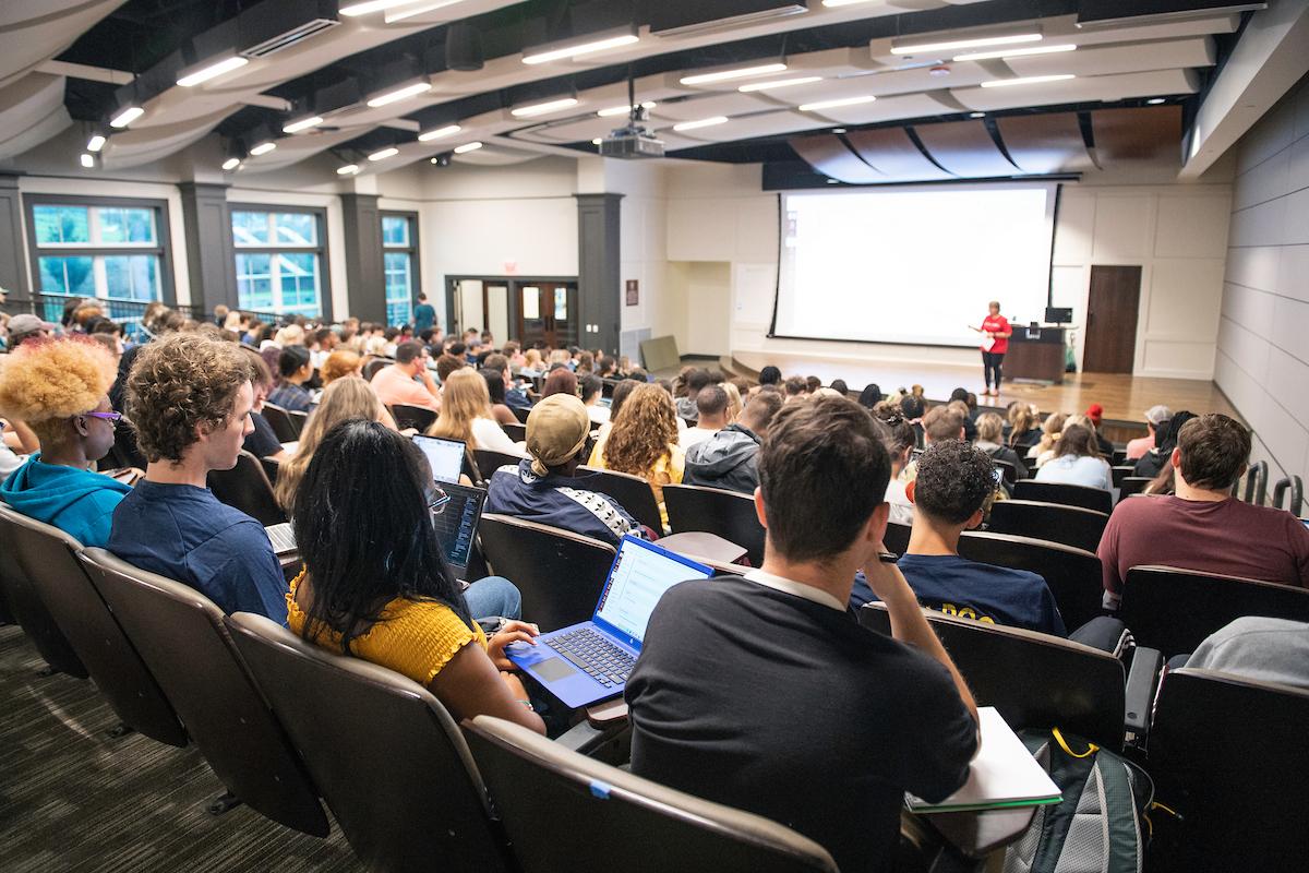 A faculty member teaches in front of a large classroom full of students.