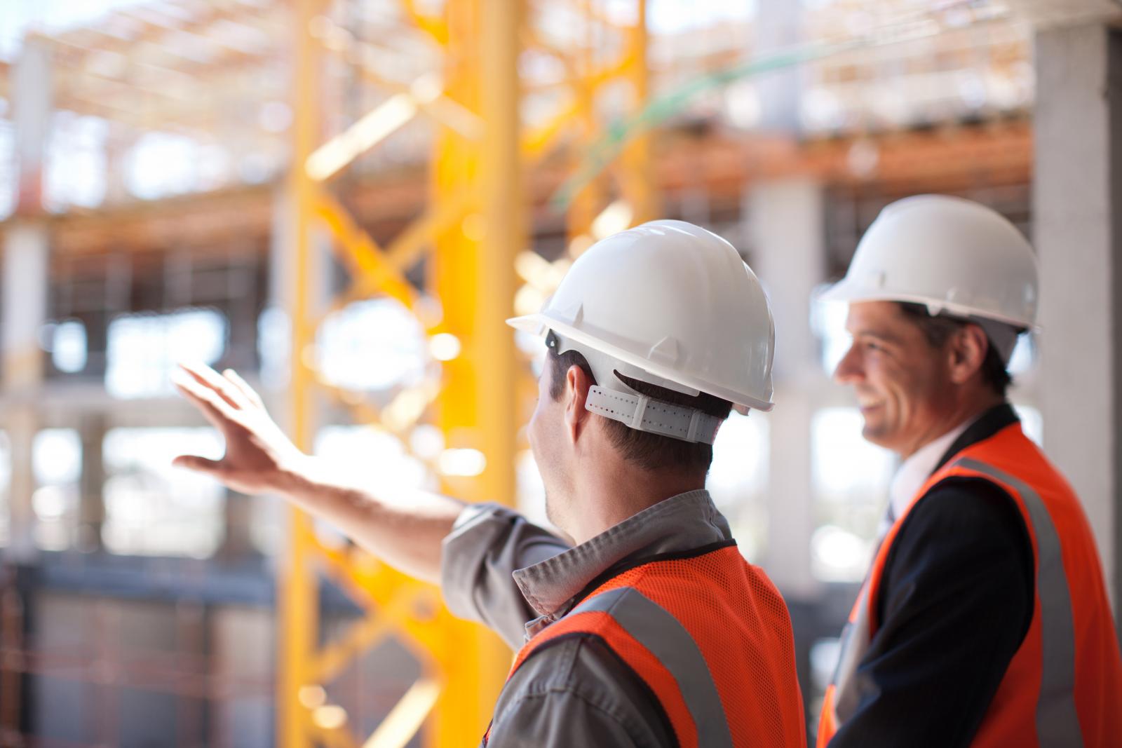 Photo of two workers in construction hats at a construction site.
