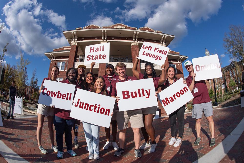 Mississippi State Roadrunners hold up their group signs in front of the YMCA Building before setting off on campus tours for prospective students and parents.