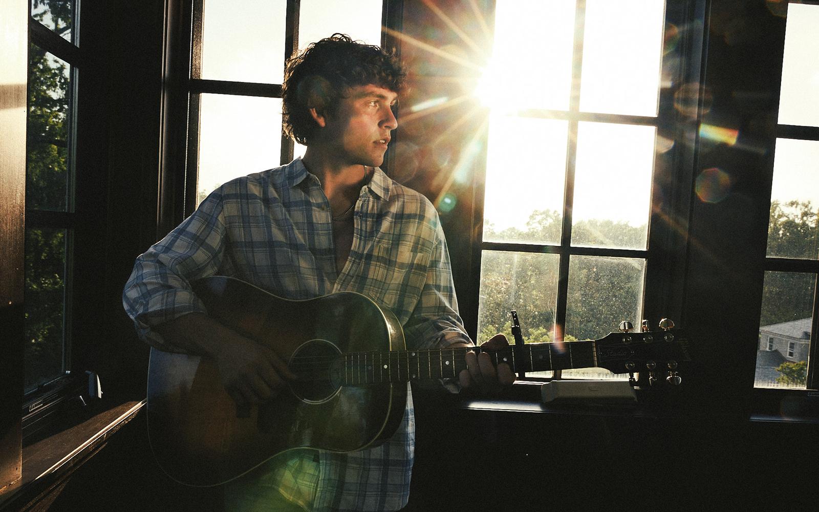 A press image of Vincent Mason playing guitar in a sun room.