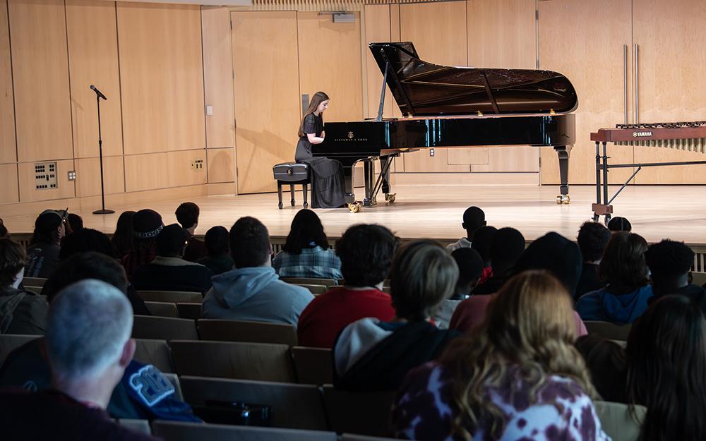 A pianist performs on stage in front of a crowded room of spectators.